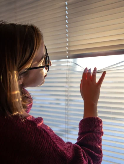 woman-looks-through-blinds-early-morning-sunlight